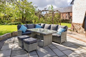 Ein Sitzbereich im Freien mit einem Korbusofa und Poufs, einem Couchtisch mit Glasplatte und einer Steinterrasse.