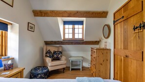 Ein Schlafzimmer mit schrägen Wänden, einem hölzernen Kleiderschrank, einem kleinen Tisch, einem Stuhl und einem Bett mit blauer Decke.