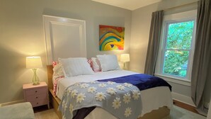 Ein Schlafzimmer mit einem Bett, zwei Nachttischen, einem Deckenventilator, einem Fenster mit Vorhängen und einem farbenfrohen, abstrakten Gemälde an der Wand.
