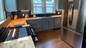 Eine moderne Küche mit einem Edelstahlkühlschrank, einer schwarzen Induktionskochplatte und Pendelleuchten.