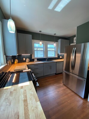 A modern kitchen with a stainless steel refrigerator, a black induction cooktop, and pendant lighting. - Designer 2 bedroom cottage minutes from downtown where luxury meets convenience. (Charlotte)