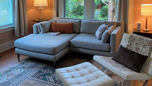 Ein Wohnzimmer mit einem Ecksofa, einem weißen Sessel, einem gemusterten Teppich und einem Deckenventilator.