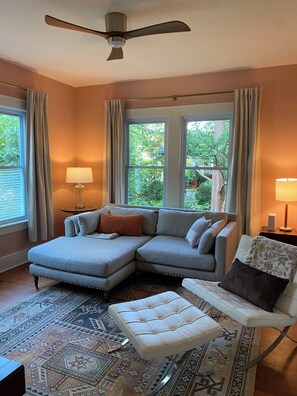 A living room with a sectional sofa, a white armchair, a patterned rug, and a ceiling fan. - Designer 2 bedroom cottage minutes from downtown where luxury meets convenience. (Charlotte)