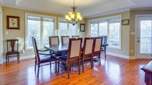 A dining room with a wooden table and chairs, a chandelier, and large windows.