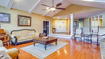 A spacious living room with hardwood flooring, a ceiling fan, a piano, and a sofa.