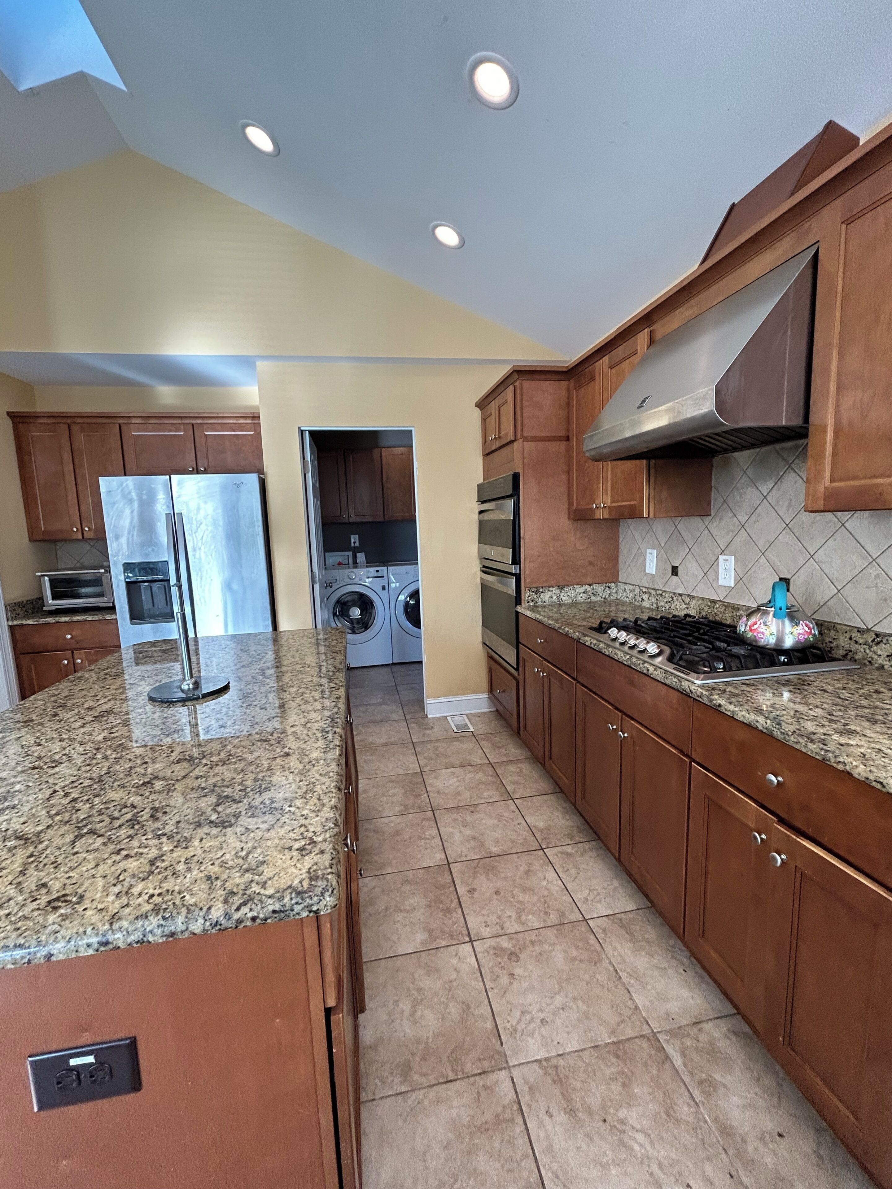 A kitchen with granite countertops, stainless steel appliances, wooden cabinets, and a tiled backsplash.