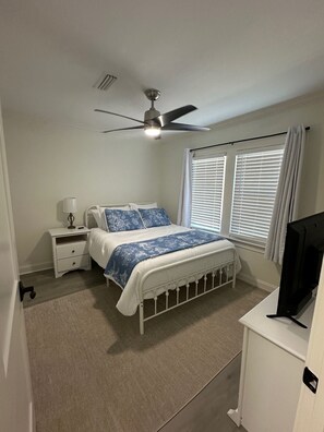 A bedroom with a bed, a nightstand, a ceiling fan, a window with blinds, and a television. - Moultrie Main Street Beauty 1125 (Moultrie)