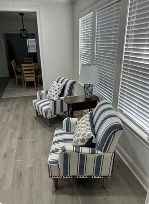 A corner seating area with two striped sofas, a small table with a lamp, and a dining area in the background. - Moultrie Main Street Beauty 1125 (Moultrie)