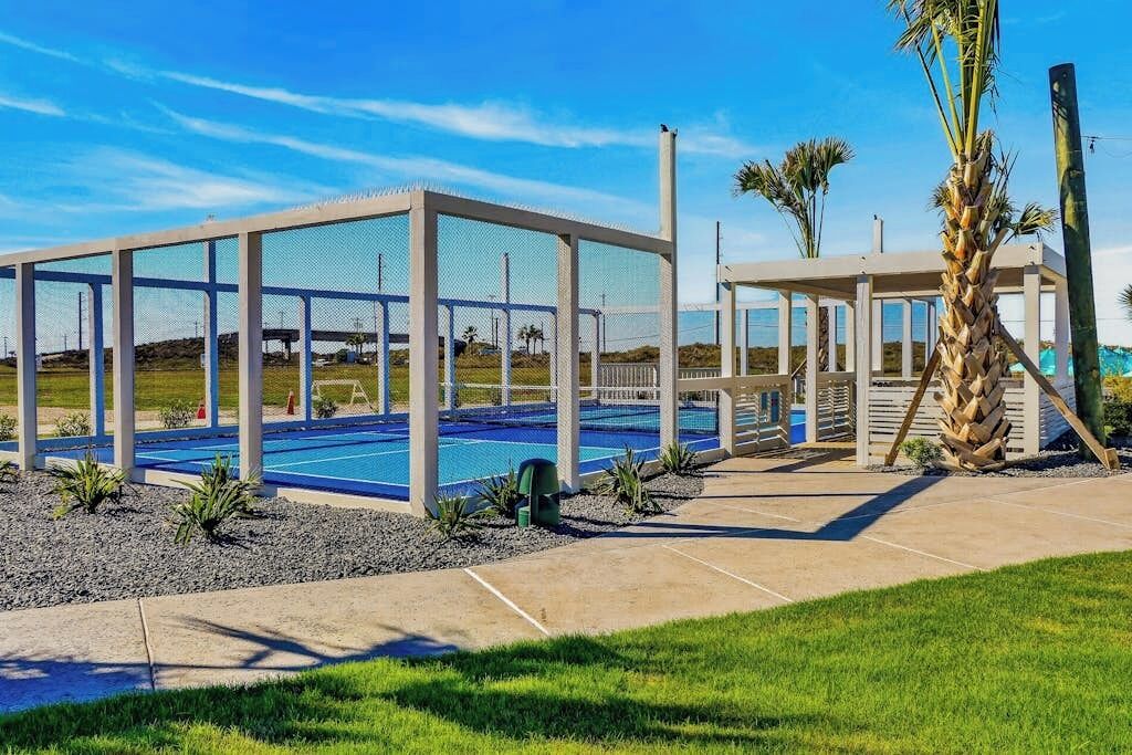 A pool area with a covered deck, palm trees, and a clear sky.