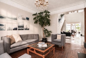 Ein geräumiges Wohnzimmer mit grauem Sofa, Couchtisch und einer großen Topfpflanze.
