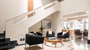 A spacious living area with a staircase, black sofas, a coffee table, and a dining area with a chandelier. - Art Deco 6-Bedroom House in Condesa with a Rooftop (Ciudad de México)