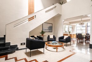 A spacious living area with a staircase, black sofas, a coffee table, and a dining area with a chandelier. - Art Deco 6-Bedroom House in Condesa with a Rooftop (Ciudad de México)