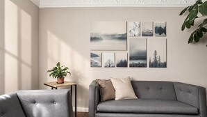 A living room with a grey sofa, a matching armchair, a small table with a potted plant, and a wall with framed artwork. - Art Deco 6-Bedroom House in Condesa with a Rooftop (Ciudad de México)