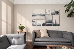 A living room with a grey sofa, a matching armchair, a small table with a potted plant, and a wall with framed artwork. - Art Deco 6-Bedroom House in Condesa with a Rooftop (Ciudad de México)