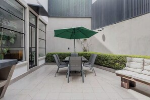 Eine Terrasse mit Tisch, Stühlen, einem grünen Sonnenschirm und einer Sitzecke.