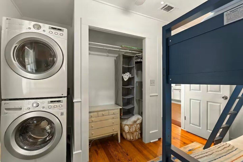 A laundry area with stacked washing machines, a storage closet, and a wooden floor.