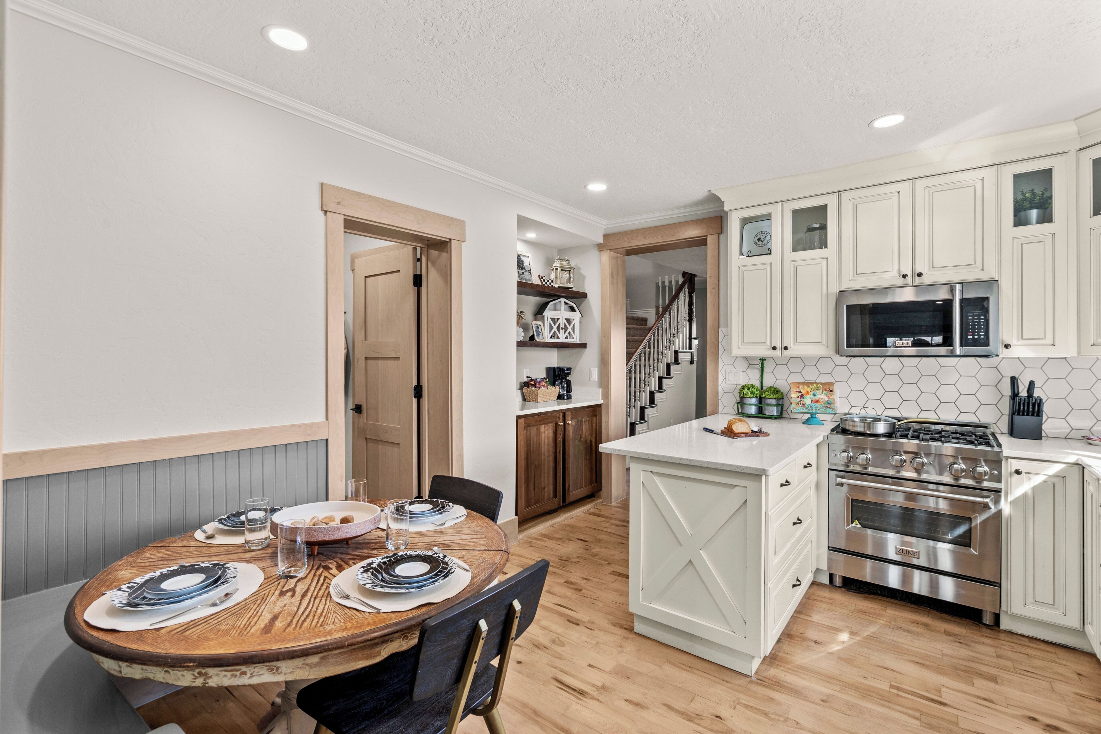 Una cocina con armarios blancos, una isla central y una zona de comedor con mesa y sillas de madera.
