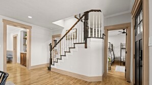 Amplia habitación con piso de madera, una escalera blanca y una puerta que da a un dormitorio.