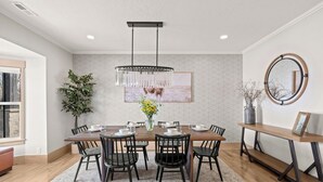 Un comedor con una mesa de madera, sillas negras, una lámpara de araña colgante y un espejo fijado a la pared.