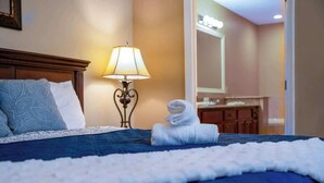Habitación de hotel con una cama bien hecha, una lámpara, una toalla doblada y un espejo.