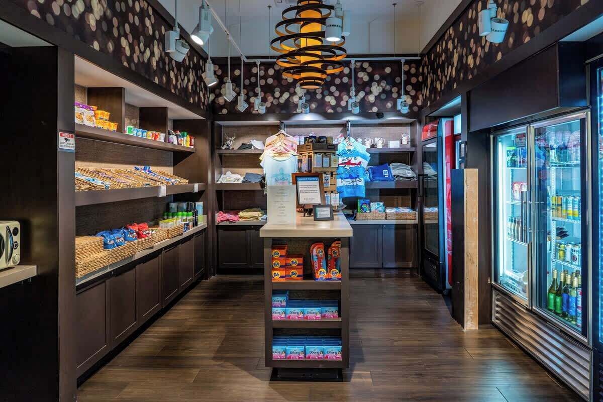 Interior de una tienda con estanterías llenas de diversos productos, un área de exhibición central y una sección refrigerada a la derecha.