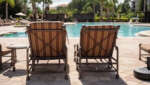 Dos sillones de descanso frente a una piscina con un patio de baldosas.