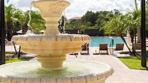 Una fuente escalonada con agua que cae, rodeada de una zona de piscina con tumbonas y palmeras.