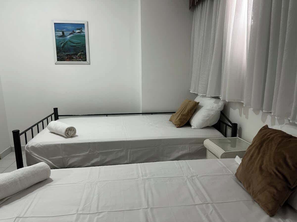 Una cama individual con colchón blanco y almohada marrón, una mesita de noche pequeña y un cuadro colgado en la pared.