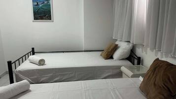 Una cama individual con colchón blanco y almohada marrón, una mesita de noche pequeña y un cuadro colgado en la pared.