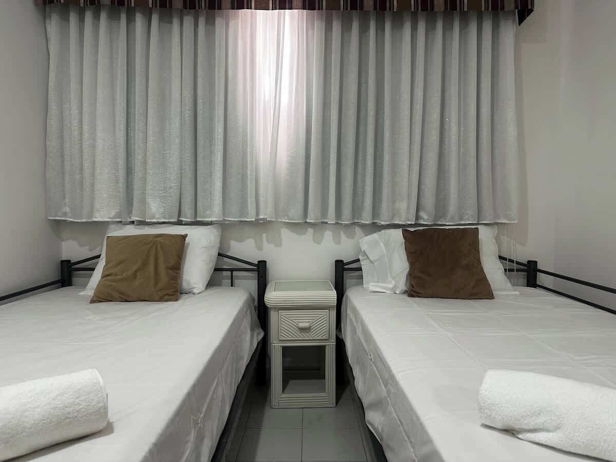 A twin room with two beds, a bedside table, and a window with curtains.