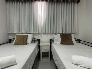A twin room with two beds, a bedside table, and a window with curtains.