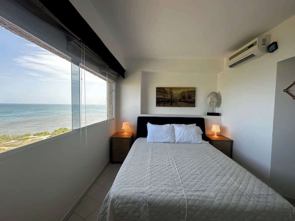 A bedroom with a large bed, two bedside tables with lamps, a ceiling fan, and a painting on the wall.