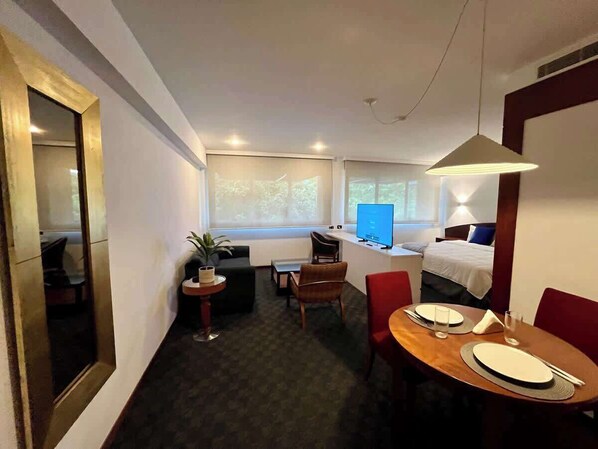 A hotel room with a dining area, a bed, a TV, and a small table with a plant. - ¡Visita caracas con estilo! Habitación en Altamira (Caracas)