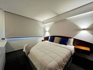 Ein modernes Hotelzimmer mit einem Bett, Nachttischen und einem Fenster mit Jalousien.