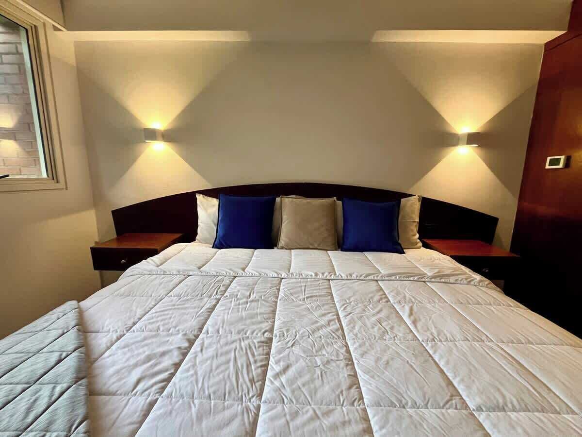 A bed with a white quilt, two bedside tables, and two wall-mounted lights.