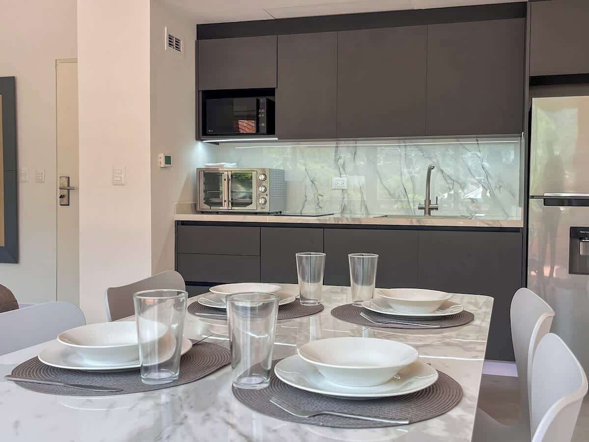 Una cocina moderna con encimera de mármol, microondas integrado y electrodomésticos de acero inoxidable.
