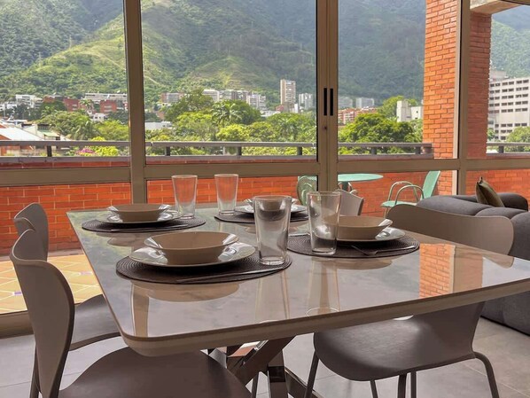 Comedor con una mesa lista para cuatro, ventanas amplias y vistas a la ciudad y colinas.