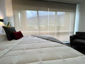 A bedroom with a large bed, a view of the outdoors through a window, and a chair.