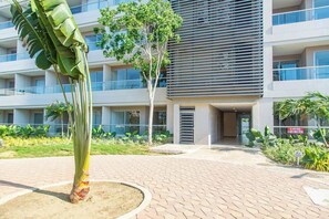 Un edificio moderno con tetto piatto, diversi balconi e un cortile lastricato con una palma e altra vegetazione.