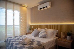 A hotel room with a bed, bedside tables, an air conditioning unit, and a view through the window. - Apto para 2 en Santa Marina Vista al mar (Santa Marta)