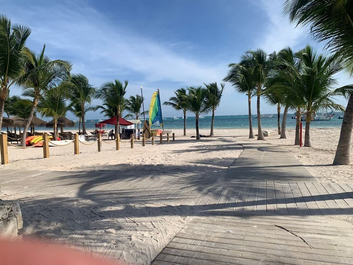 Une plage avec une promenade en bois, des palmiers et des parasols de plage.