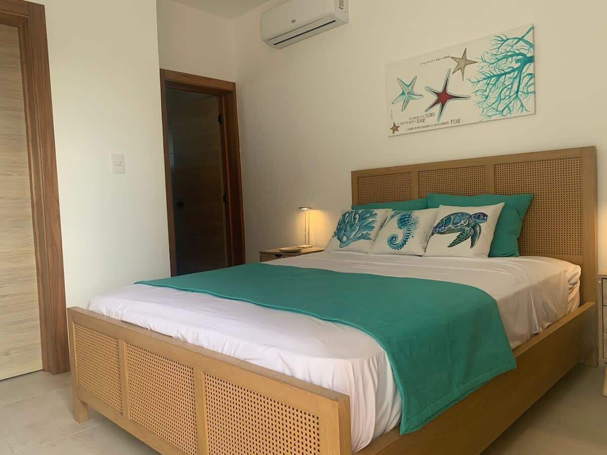 A bedroom with a bed, a nightstand, a wall-mounted air conditioner, and a door.