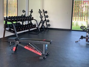 Uma academia com equipamentos de musculação, incluindo halteres e um banco.