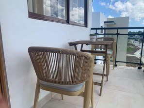 Varanda com cadeiras de vime e uma mesa, com vista para um edifício moderno e um céu limpo.