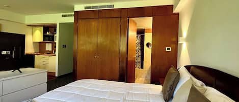 A hotel room with a large bed, a television, a wardrobe, and a kitchenette.