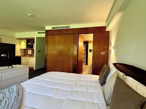 A hotel room with a large bed, a television, a wardrobe, and a kitchenette.