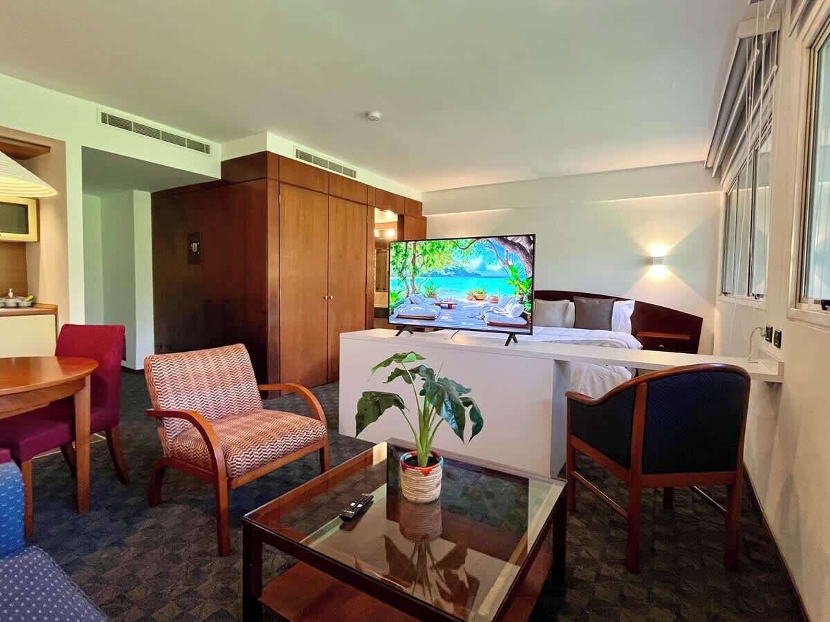 Una camera d'hotel con televisione, un tavolo da pranzo, sedie, un divano e una pianta.