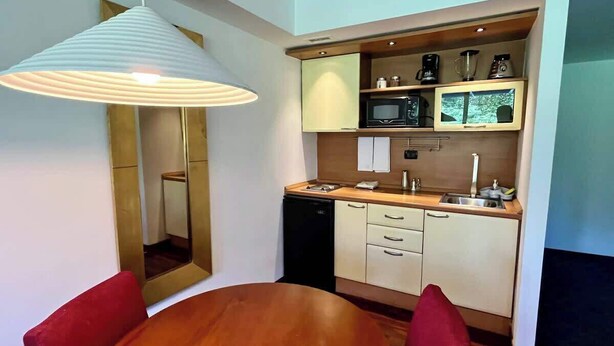 A compact kitchen with a microwave, coffee maker, and a sink. There is a dining table with chairs and a pendant light above it. - Hogar en Altamira Acogedor y en el Corazón de Todo (Caracas)