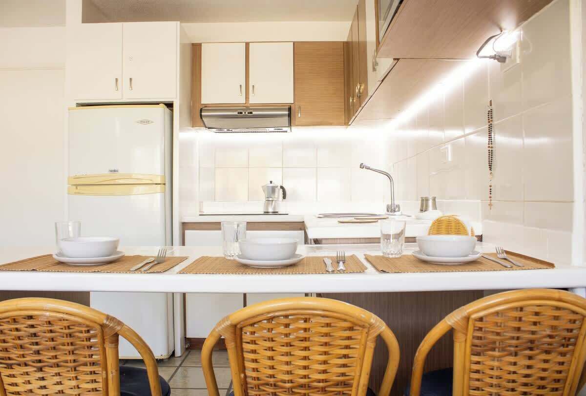 Eine moderne Küche mit weißen Schränken, einem Edelstahlkühlschrank, einem Einbauofen und einem Essbereich mit einem weißen Tisch und Korbstühlen.
