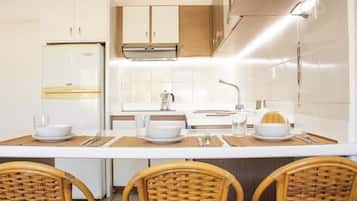 Eine moderne Küche mit weißen Schränken, einem Edelstahlkühlschrank, einem Einbauofen und einem Essbereich mit einem weißen Tisch und Korbstühlen.